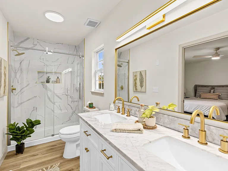 Marble walk-in shower and double vanity with gold fixtures and window light opening through to the bedroom