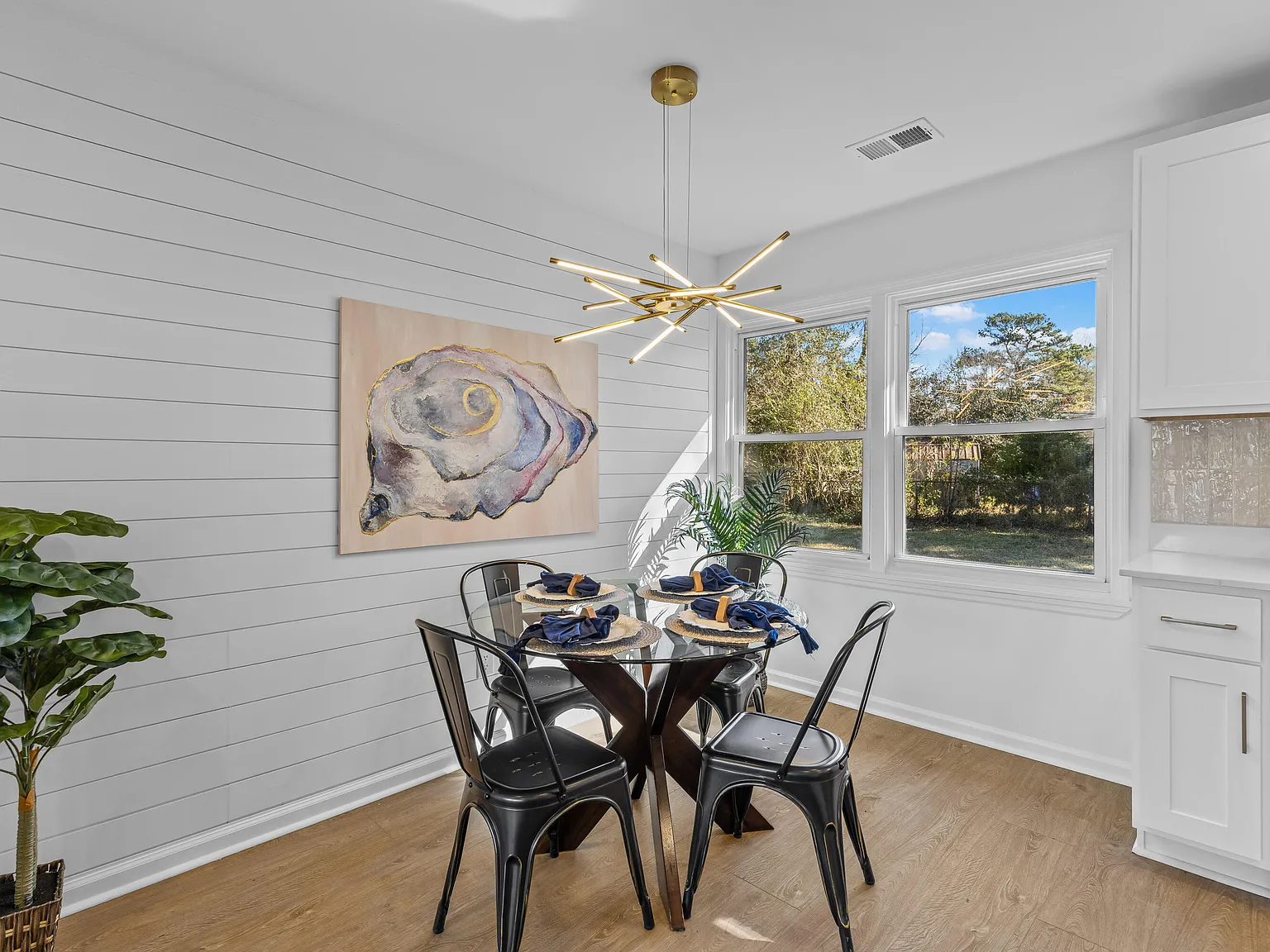 Shiplap dining nook with still-life art and black metal bistro chairs