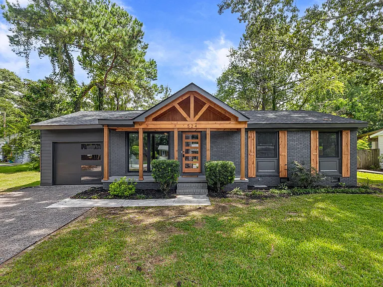 Gray ranch with a cedar gable framed by trees at dusk