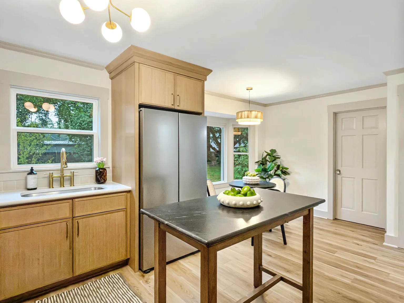 Light-oak kitchen with a brass globe sputnik light, gold bridge faucet, soapstone island, and a sunny breakfast nook