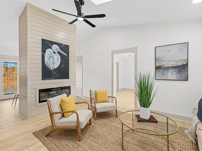 Sunlit vaulted living room with a floor-to-ceiling shiplap fireplace, mustard pillows, a jute rug and a blue heron painting.