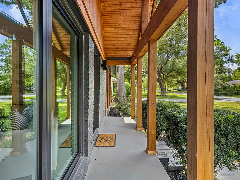 Looking down a covered porch with a warm cedar tongue-and-groove ceiling, gray brick, and floor-to-ceiling glass opening to a green lawn