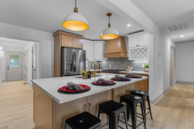 Open kitchen with a wood-tone island, white quartz counters, glass pendant lights, and a sage stacked-tile backsplash.