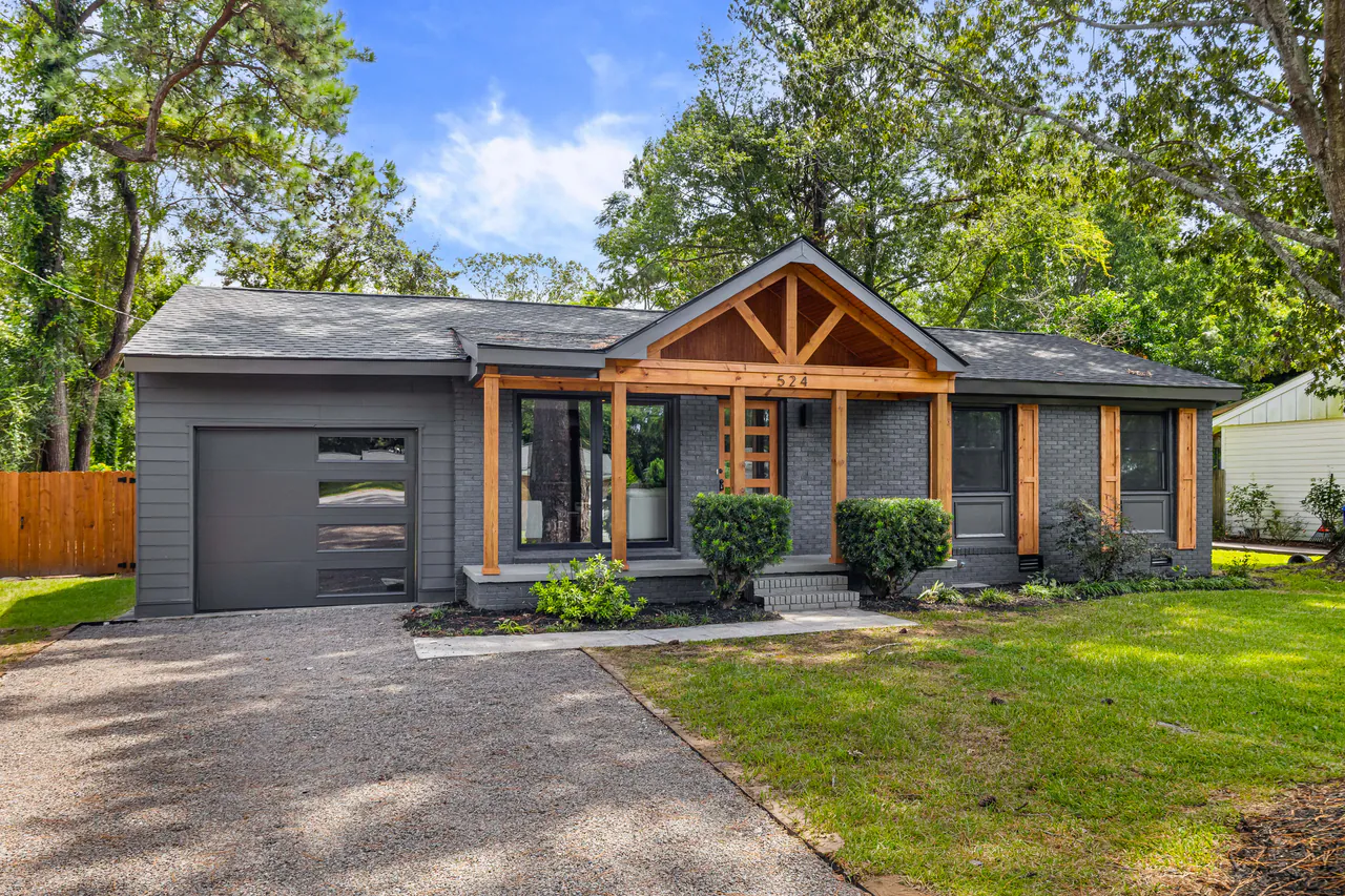 Gray-brick ranch with a cedar timber porch gable, cedar posts, a frosted-glass garage door, and a manicured lawn under a clear blue sky.