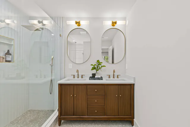 Spa bath with a walnut double vanity, marble tops, brass fixtures, round mirrors, and a glass walk-in shower.