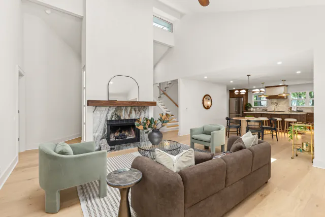 Open great room with a vaulted ceiling, a stone fireplace with a wood mantel, and sage accent chairs.