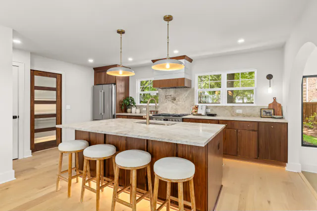 Kitchen with walnut cabinetry, a marble waterfall island, wood-and-white stools, and glass pendant lights.