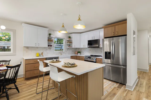 Renovated kitchen with white upper cabinets, wood lowers, a white quartz island with stools, and a dining nook.