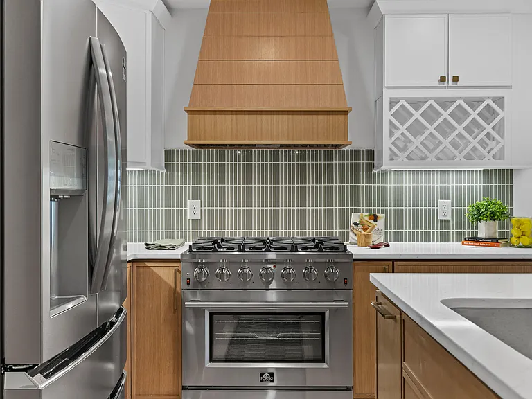 Tight detail of a stainless pro range under a wood slat hood with a sage stacked-tile backsplash and white lattice wine rack