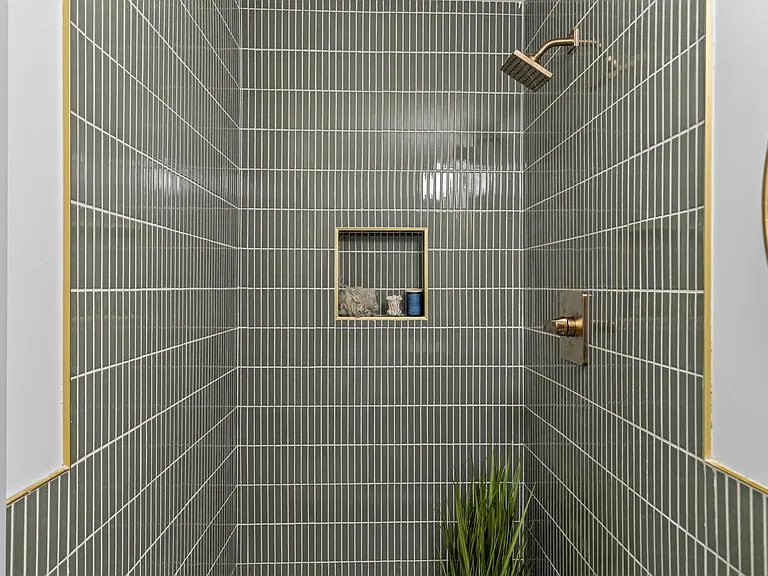 Detail of deep-sage vertical stacked shower tile with a brass rain head and niche